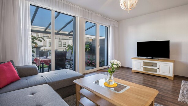 Een moderne woonkamer met een bank, een salontafel, een televisie en grote ramen.