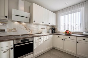 Une cuisine moderne avec des meubles blancs, un four encastré et un dosseret en marbre.