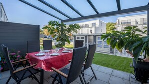 Een terras buiten, met een eettafel en stoelen, omringd door potplanten.