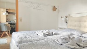 Makuuhuoneessa on sänky, tuoli, seinälle ripustettu kori ja taustalla pieni keittiönurkkaus.