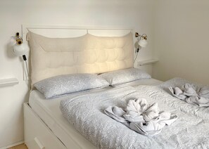 Un lit doté d’une tête de lit capitonnée, de draps à motifs et de serviettes disposées sur le lit.