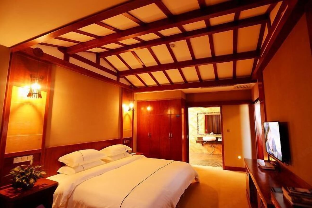 A hotel room with a large bed, wooden ceiling beams, a television, and a bathroom visible through an open door.
