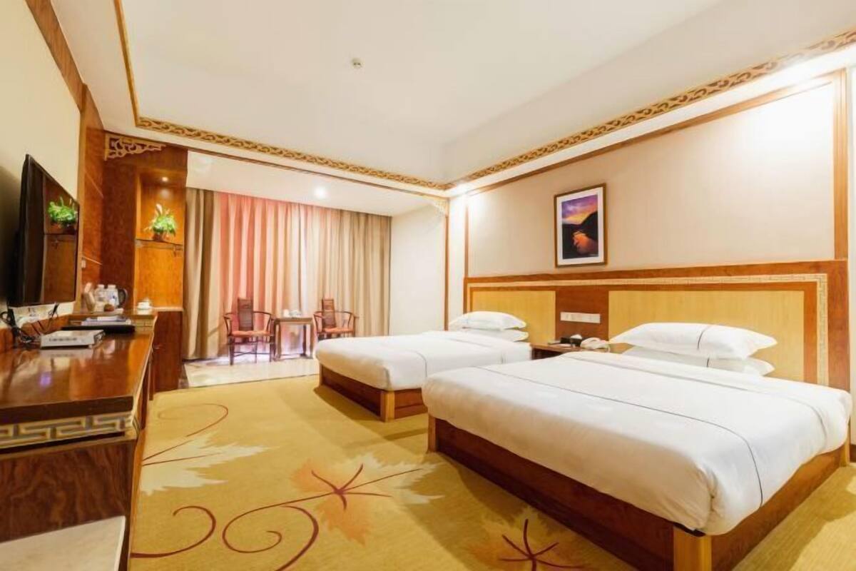 A hotel room with two beds, a desk with a flat-screen TV, a small table, and a chair.