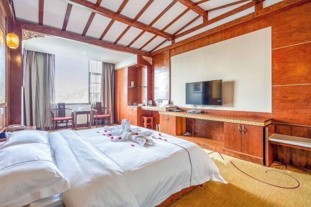 A hotel room with a large bed, a TV, wooden furniture, and a view of the outdoors.