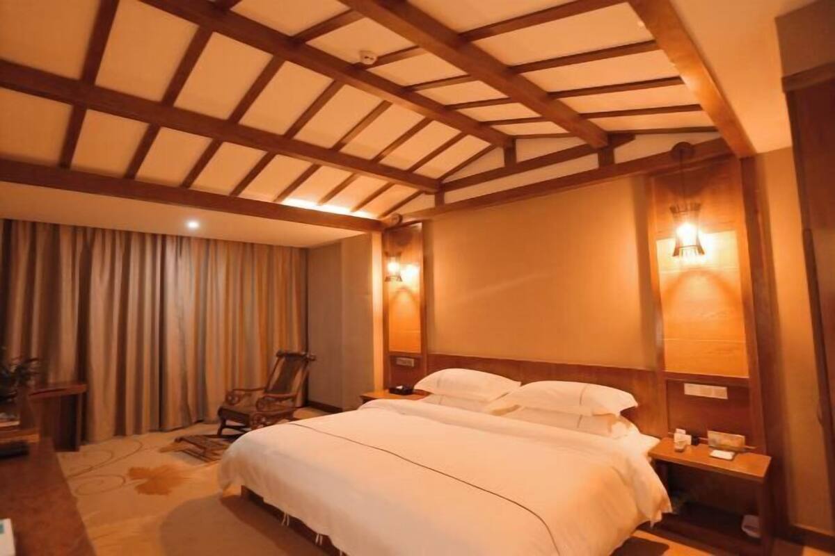 A hotel room with a wooden ceiling, a large bed, two bedside tables, and a chair.