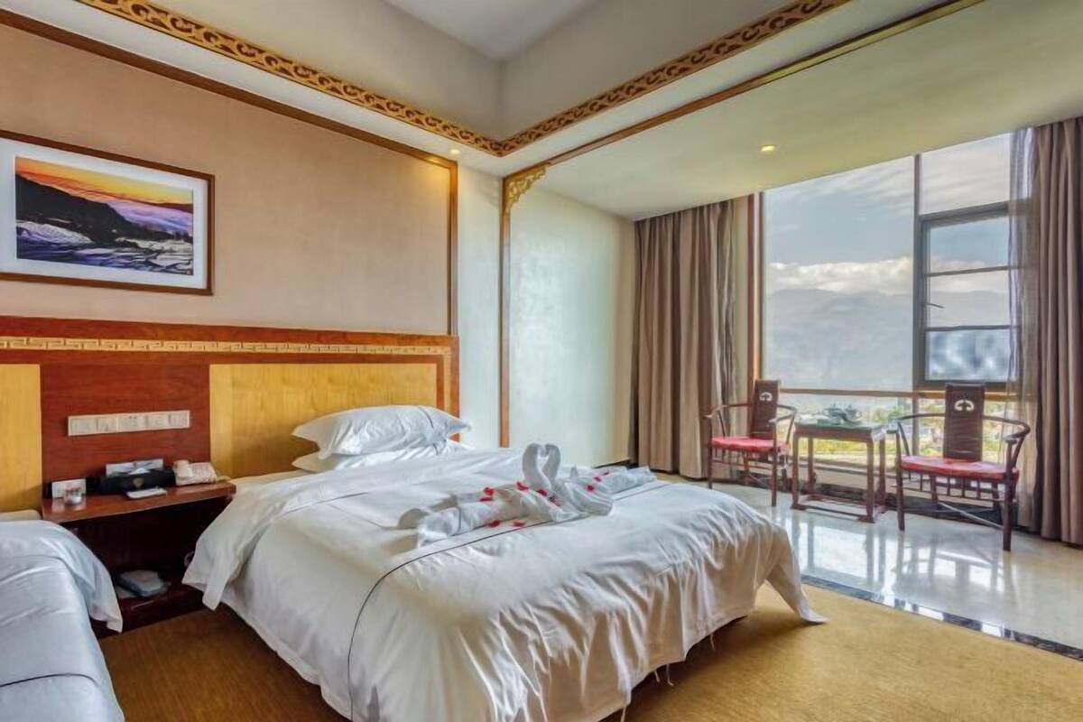 A hotel room with a large bed, a desk with a telephone, a chair, and a view of the outdoors.