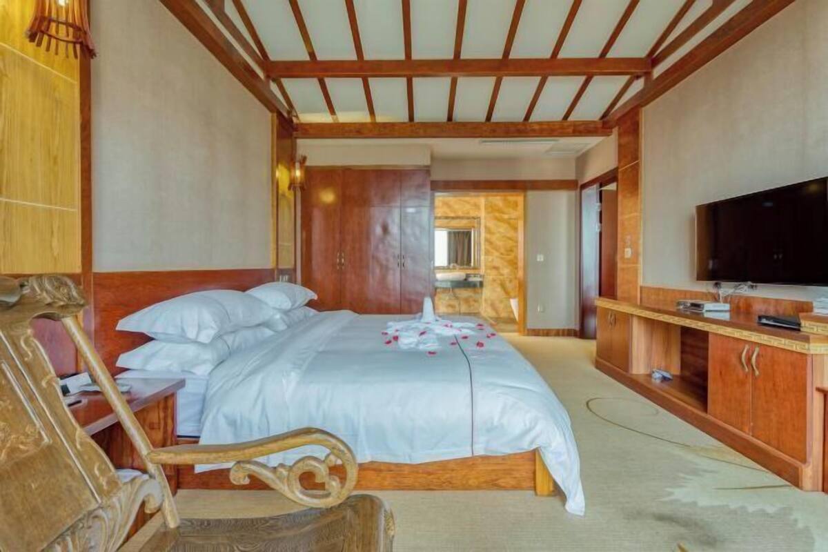 A bedroom with a wooden ceiling, a bed with white bedding, a wooden nightstand, a TV, and a wooden wardrobe.