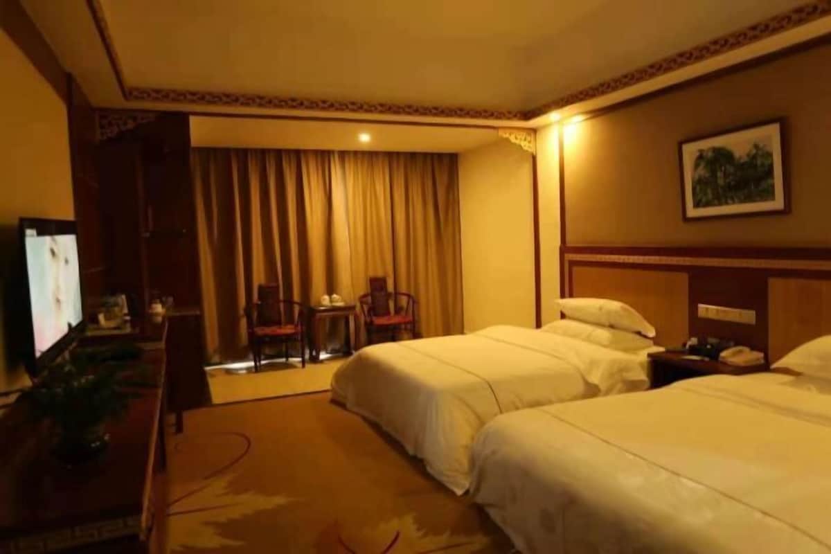 A hotel room with two beds, a television, a desk with a chair, and a window with curtains.