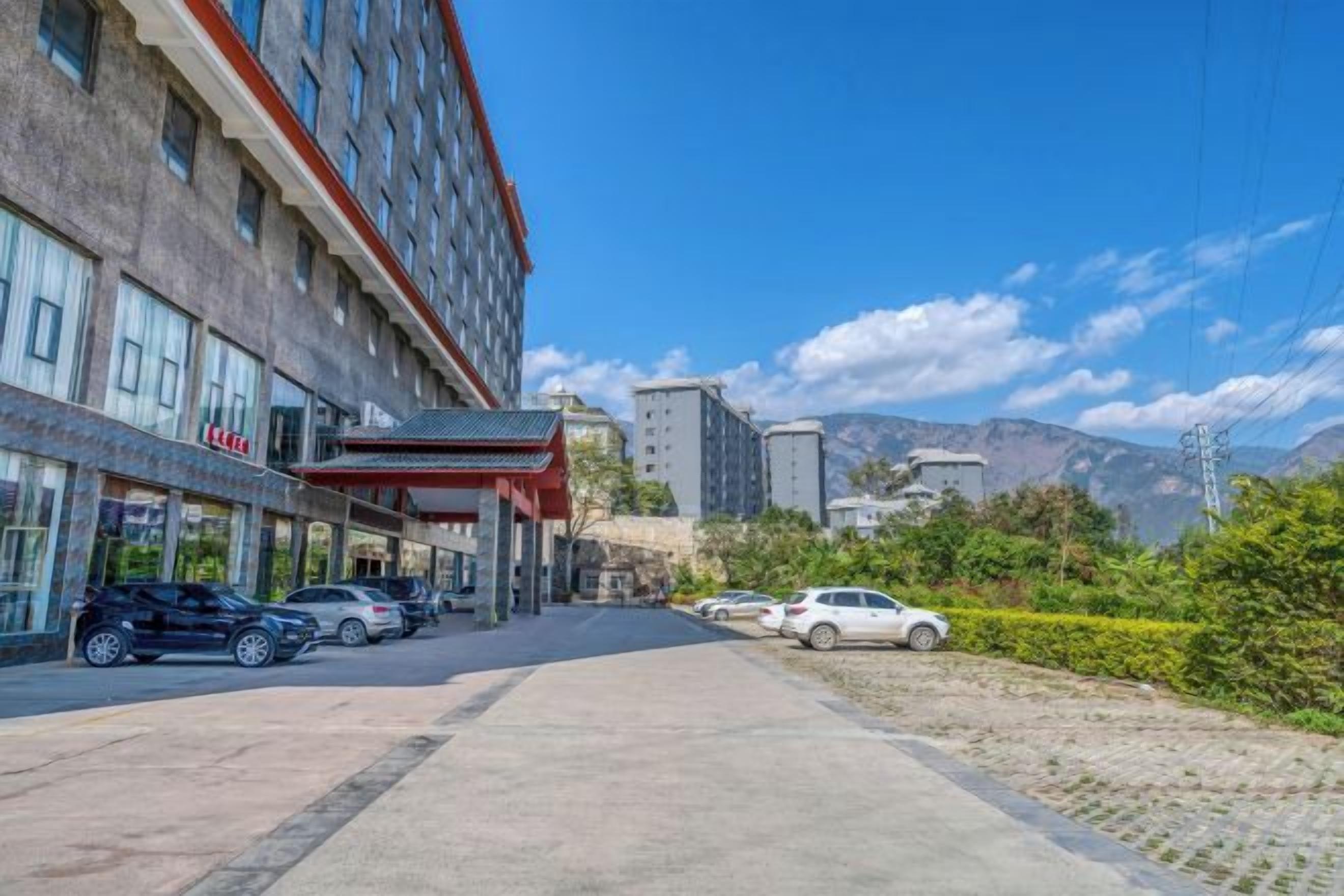 Um hotel com estacionamento, entrada coberta e vista para montanhas ao fundo.
