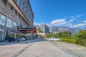 A hotel with a parking lot, a covered entrance, and a view of mountains in the background. - Yunti Hotel (Honghe County)