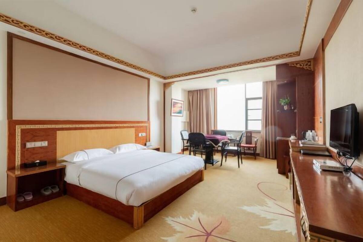 A hotel room with a large bed, a desk with a chair, a television, and a window with curtains.