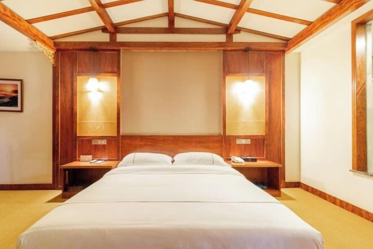 A hotel room with a large bed, wooden headboard, two bedside tables with lamps, and a wooden ceiling structure.