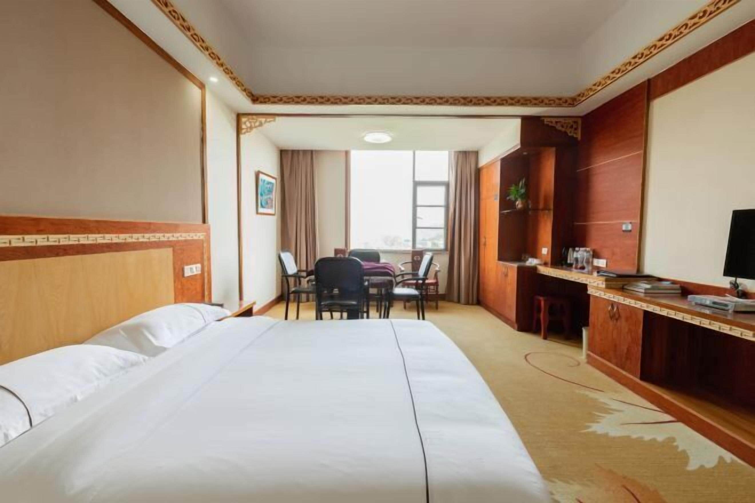 A hotel room with a large bed, a desk, a chair, and a television.