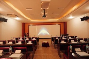 A conference room with rows of tables, a projector screen, and a ceiling-mounted projector. - Yunti Hotel (Honghe County)