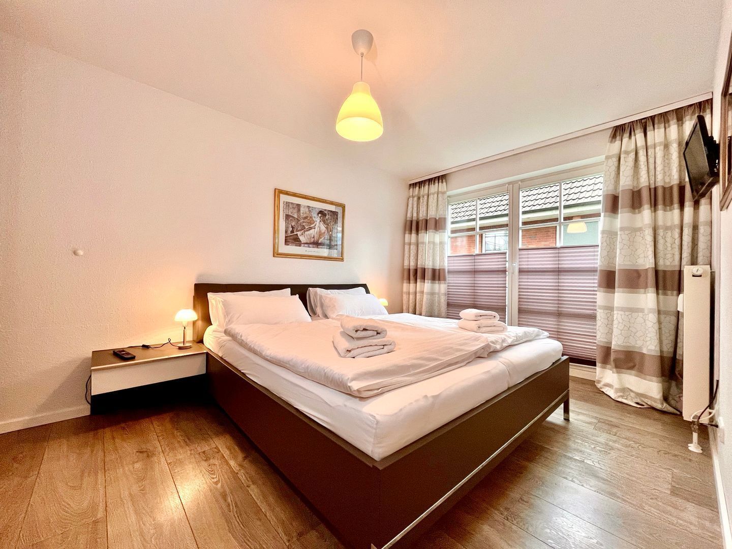 A hotel room with a bed, bedside table, lamp, picture on the wall, and a window with curtains.