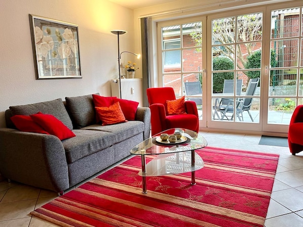 A living room with a grey sofa, red armchair, and glass coffee table.