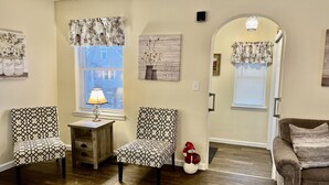 Una sala de estar con dos sillones estampados, una mesita con lámpara, un sofá y un muñeco de nieve decorativo.