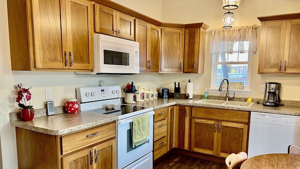 Una cocina con armarios de madera, un microondas blanco, una estufa, un lavabo y una cafetera.