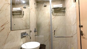 A modern bathroom with a glass-enclosed shower, a white toilet, and a marble-tiled wall. - HOTEL XENIA (Varanasi)