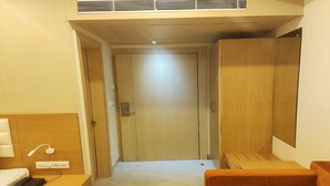 A hotel room with a bed, a nightstand with a phone, a wooden wardrobe, and a sofa. - HOTEL XENIA (Varanasi)