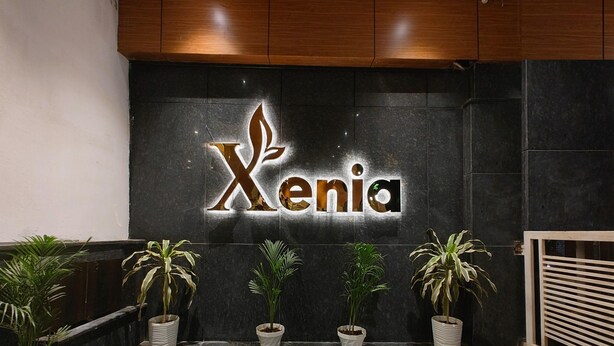 A reception area with a dark tiled wall and a sign that reads "Xenia". - HOTEL XENIA (Varanasi)