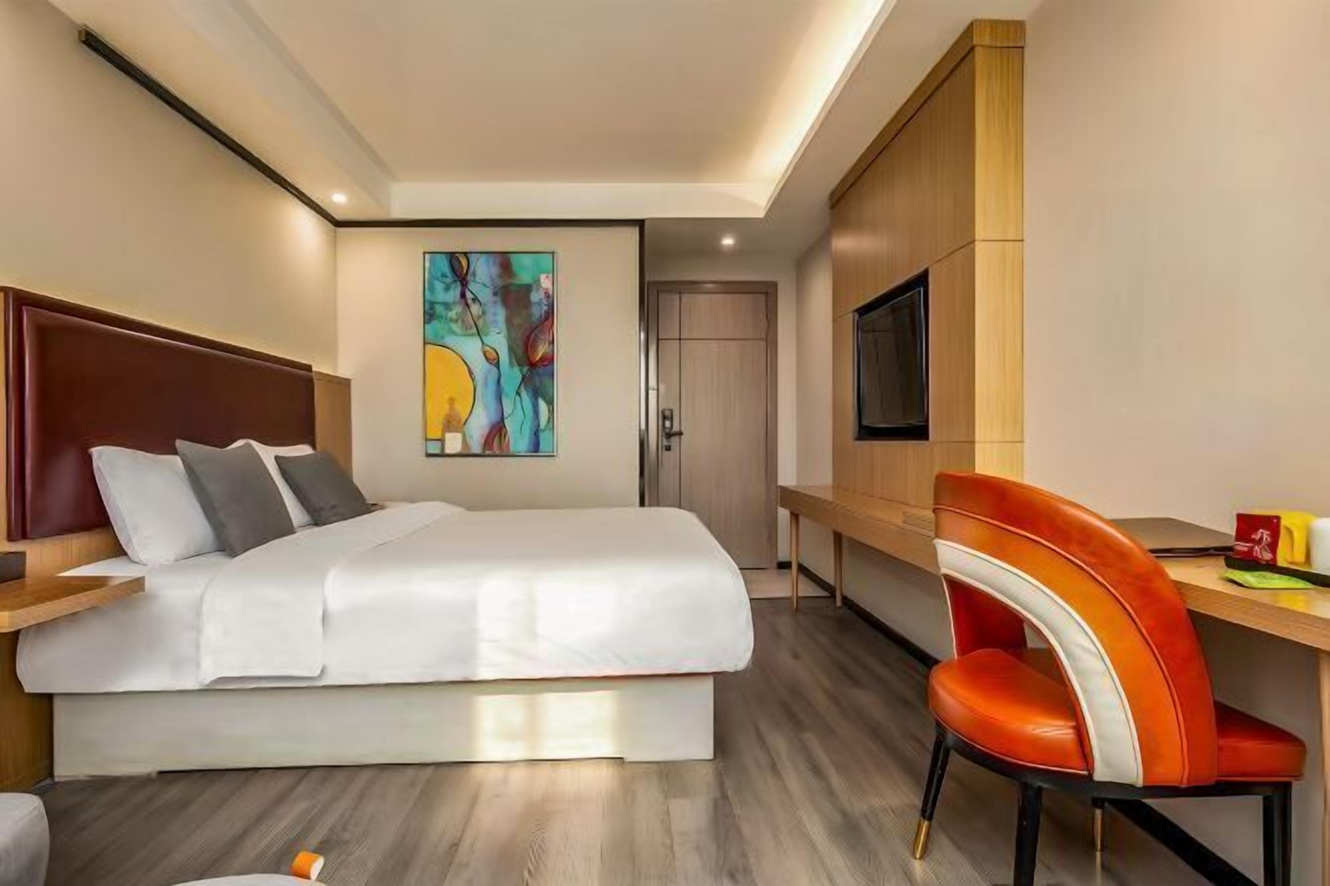 A hotel room with a bed, a desk, a chair, a TV, and a painting on the wall.
