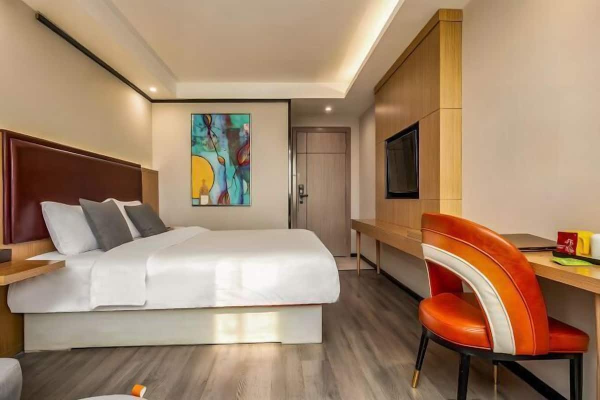 Une chambre dâhĂŽtel avec un lit, un bureau, une chaise, une tĂ©lĂ©vision et un tableau au mur.