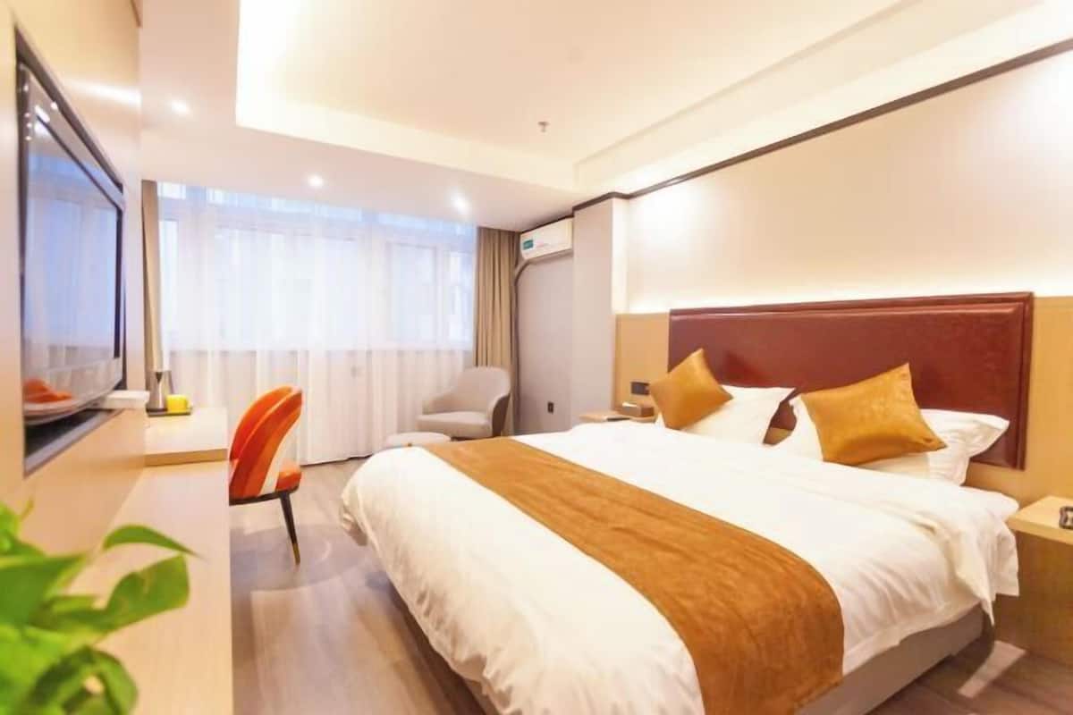 A hotel room with a large bed, a desk, a chair, and a television.