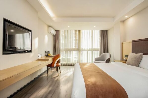 A hotel room with a bed, a desk, a chair, a TV, and large windows.