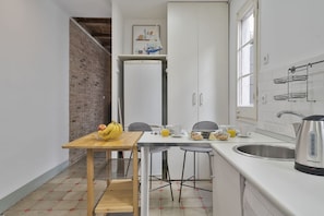 Une cuisine compacte comprenant un réfrigérateur, une table à manger avec des chaises, un évier et une bouilloire.