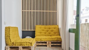 Twee gele fauteuils op houten pallets, een wand van verticale houten latten, en een groene deur met een raam.