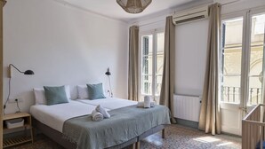 Een hotelkamer met een bed, nachtlampjes, een raam met gordijnen, een radiator en een kamer met een patroon vloer.