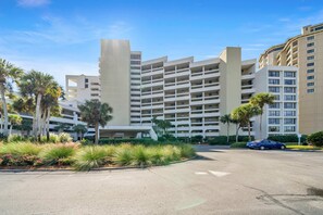 A multi-story hotel with a central courtyard, palm trees, and a parking area. - Beachside One 4067 | Gulf Front! 2PM Check in! Spectacular Gulf Front Unit with Gorgeous Decor only steps from the beach! (Miramar Beach)