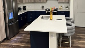 A modern kitchen with a central island, stainless steel appliances, and dark blue cabinets. - Cozy 2- bedroom with Smart TV’s, AC, WiFi, huge pool in amazing Area of Addison (Addison)