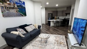 A modern living room with a dark sofa, a round coffee table, and a large TV. - Cozy 2- bedroom with Smart TV’s, AC, WiFi, huge pool in amazing Area of Addison (Addison)