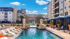 A swimming pool with lounge chairs and a covered area, surrounded by multi-story buildings. - Cozy 2- bedroom with Smart TV’s, AC, WiFi, huge pool in amazing Area of Addison (Addison)
