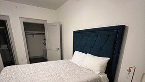 A neatly made bed with a dark headboard, a bedside table with a lamp, and a closet with a door open. - Cozy 2- bedroom with Smart TV’s, AC, WiFi, huge pool in amazing Area of Addison (Addison)