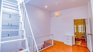 Una escalera con barandillas blancas que conduce a una habitación con piso de madera, un aparador blanco y una puerta con cortina.