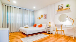 Un dormitorio moderno con una cama blanca, almohadas naranjas, un escritorio con silla y un espejo redondo.