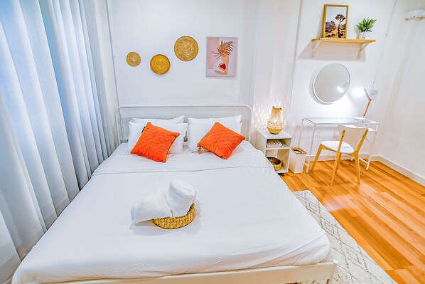 Une chambre à coucher bien rangée, avec un lit, des oreillers, une table de chevet, une chaise, un bureau et un miroir.