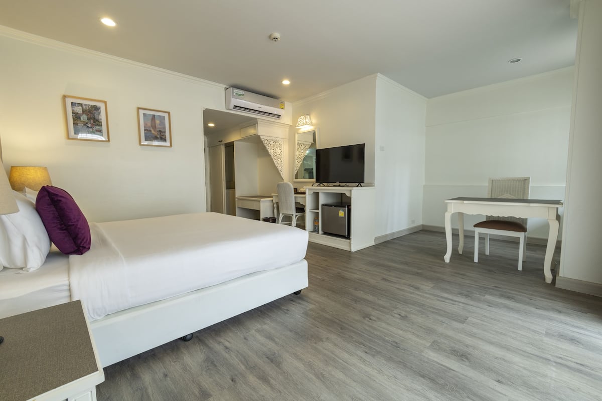 A modern hotel room with a large bed, a desk, a TV, and an air conditioning unit.