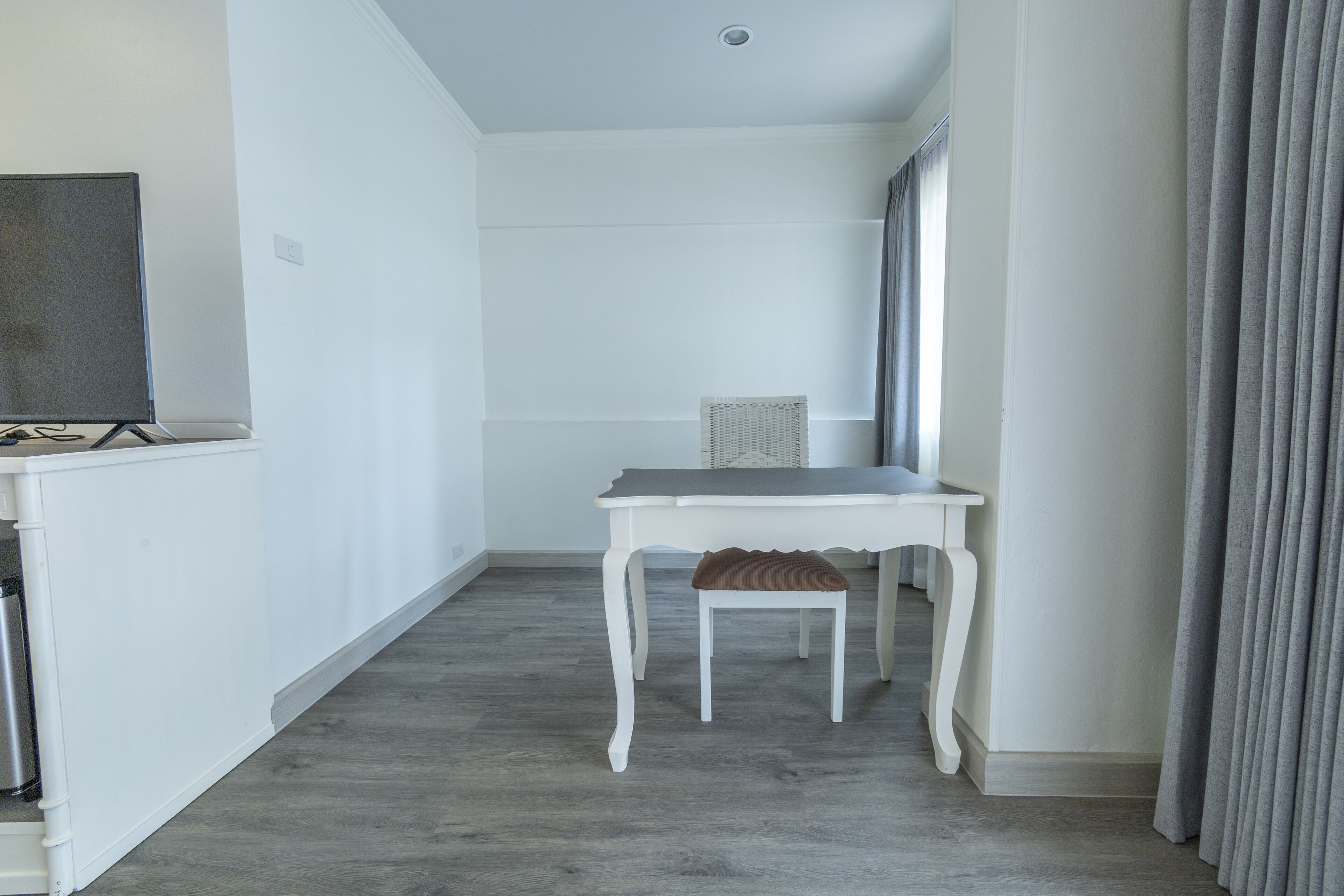 A narrow hallway with a white table and chair, a radiator, and a television on a stand.
