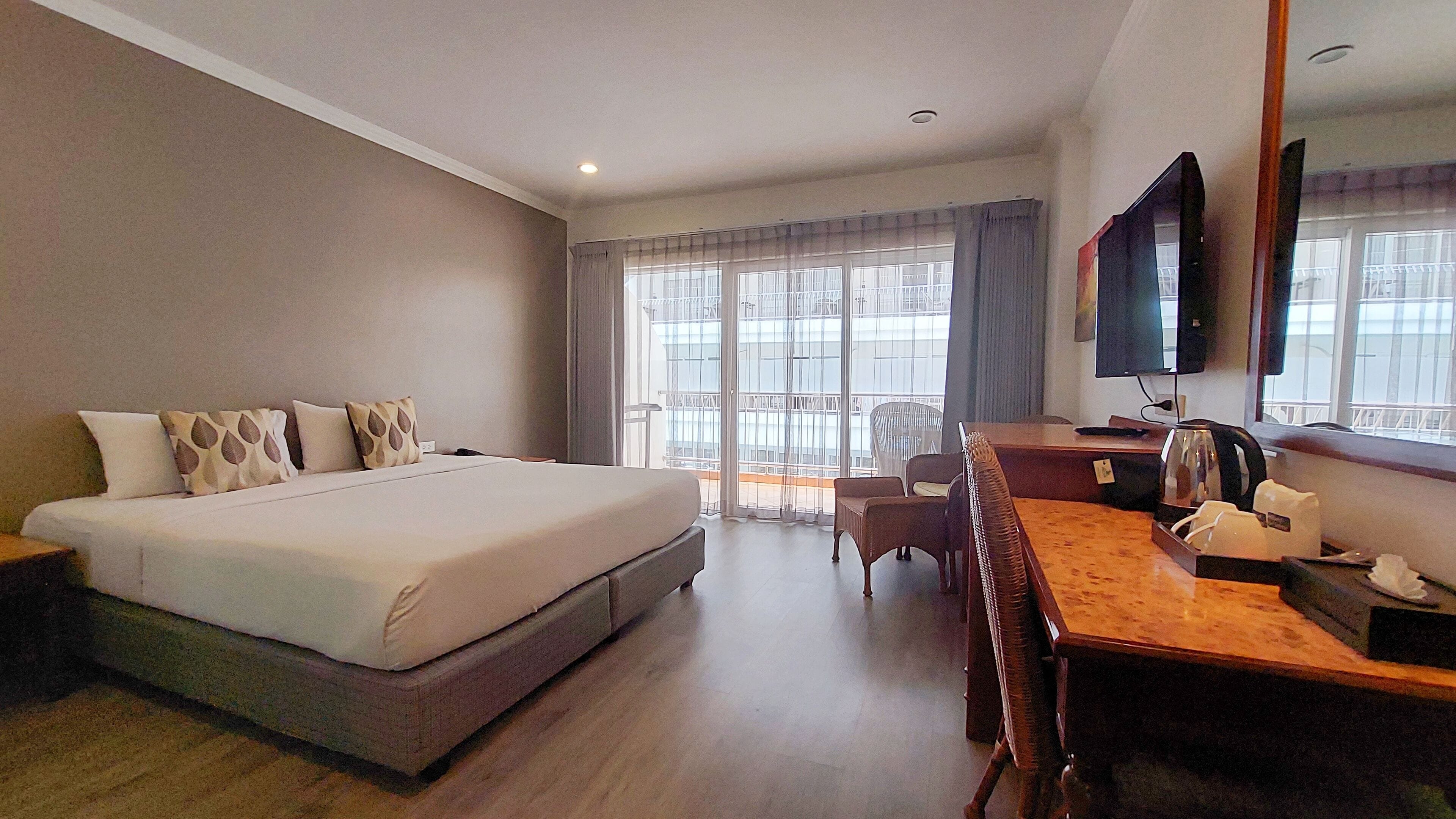 A hotel room with a large bed, a desk, a chair, and a TV.