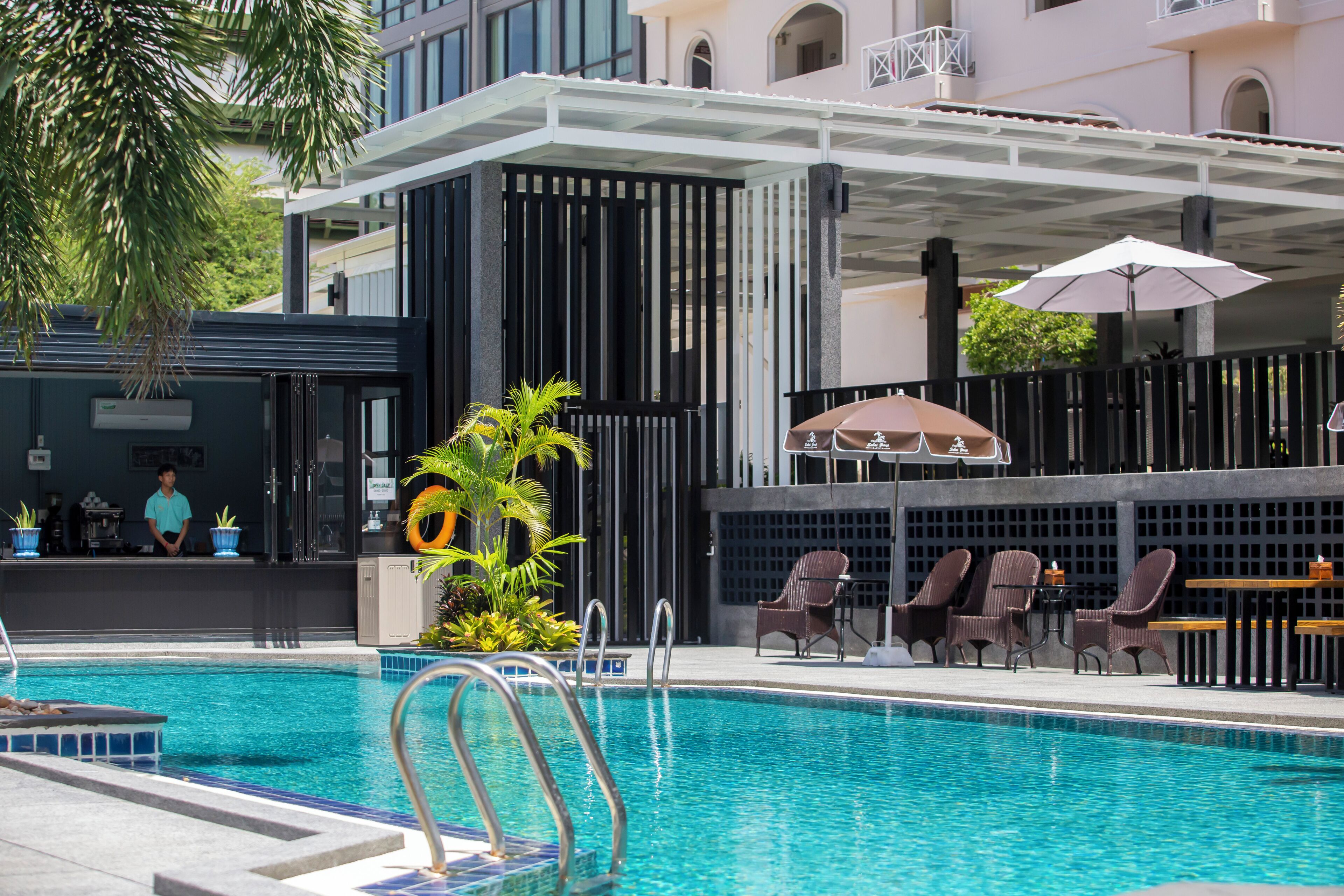 Una piscina con sillas de descanso y sombrillas, rodeada por un edificio con un porche cubierto.