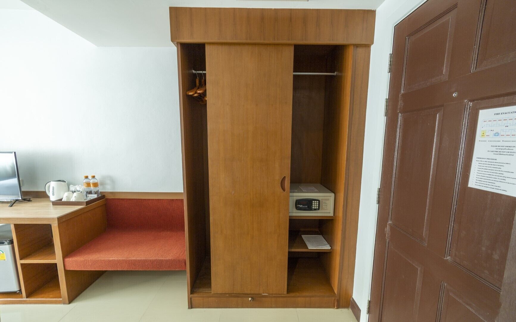 Une pièce comprenant une armoire en bois, un bureau avec un ordinateur, une chaise rouge et un petit réfrigérateur.