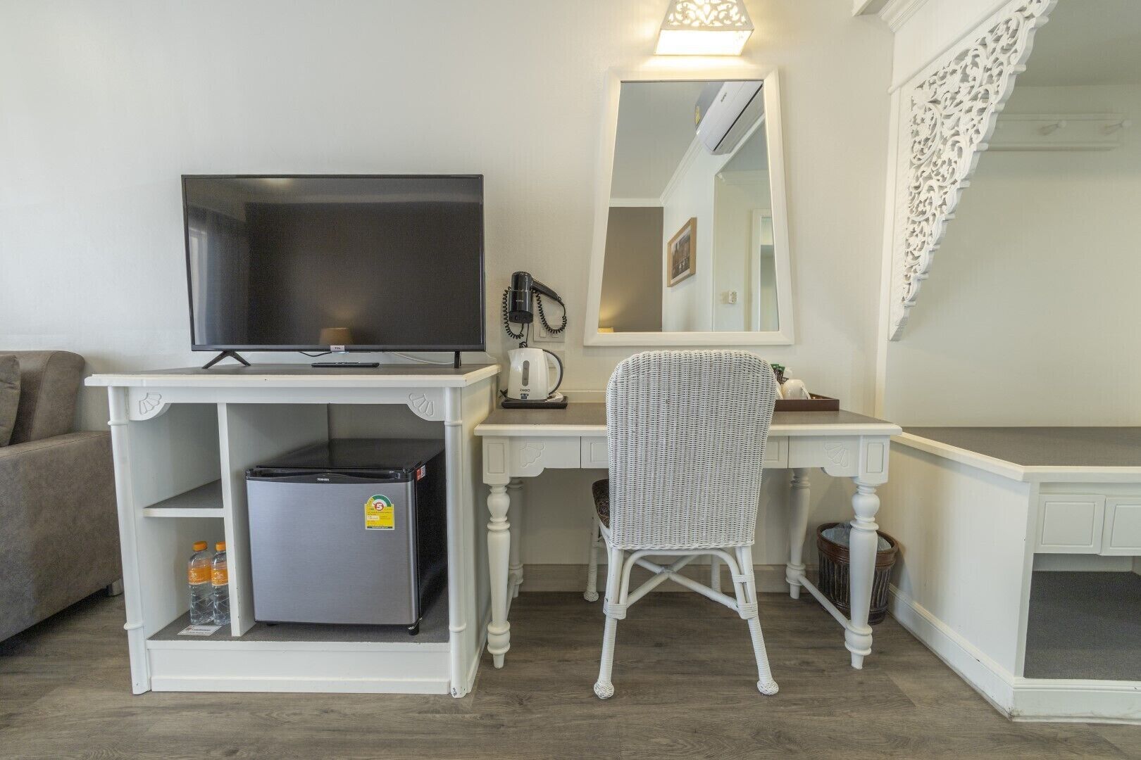Habitación compacta con televisor, refrigerador pequeño, una silla, escritorio con espejo y un adorno blanco en la pared.