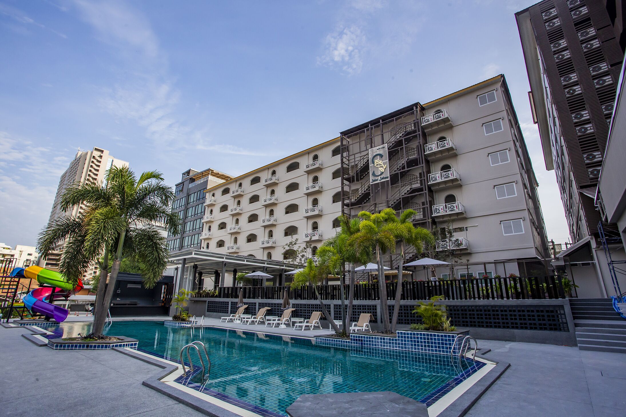 A hotel with a swimming pool, outdoor seating, and a playground.
