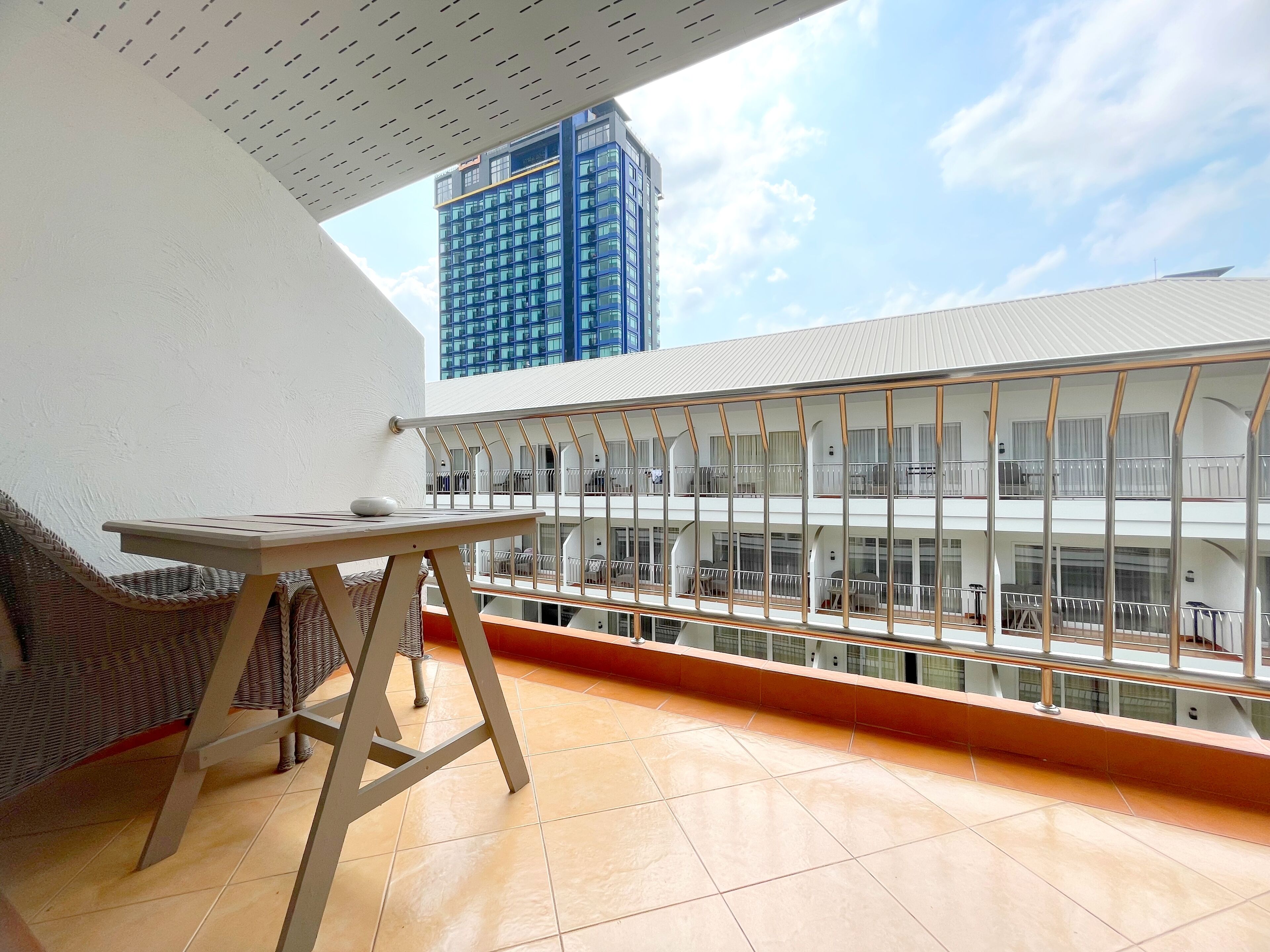 A balcony with a table and chairs, a view of a modern building, and a tiled floor.