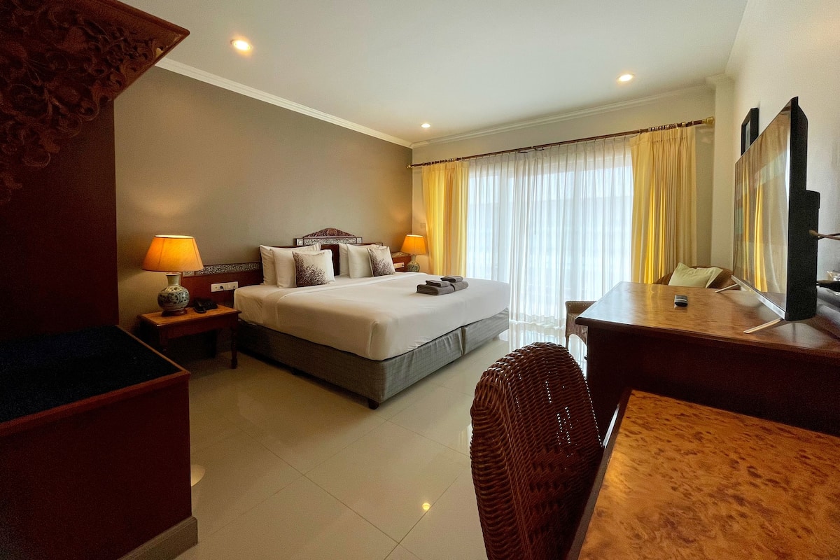 A hotel room with a bed, bedside tables, a desk, a chair, and a large mirror.