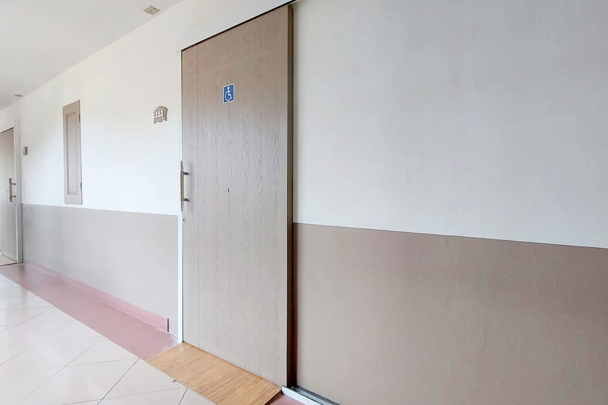 A hallway with a door marked with a wheelchair accessibility sign, a small window, and a tiled floor.